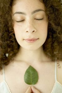 Woman with her eyes closed in calm holding a green leaf