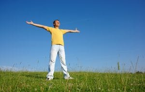 Happy young man in casual on the meadow, smile spreading his arms, summer sunny day